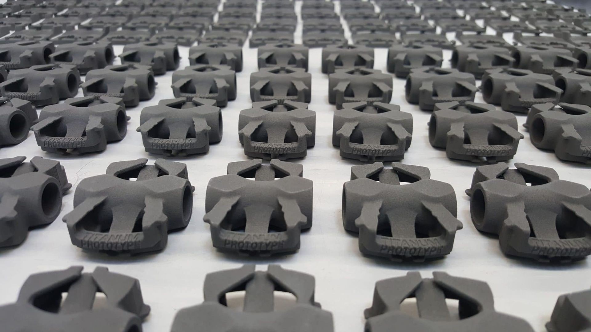 Rows of identical gray 3D-printed titanium prototypes arranged on a flat surface.