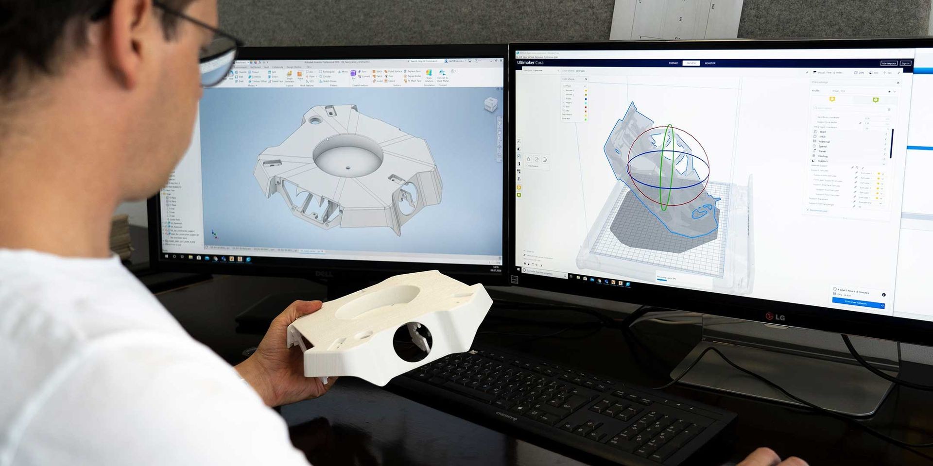 Person designing a 3D model on dual monitors while holding a 3D printed part.